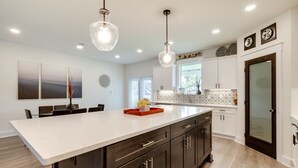 A modern kitchen with a large island, dark cabinets, and pendant lighting. - Luxe Gulf Breeze Vacation Rental: Furnished Patio! (Gulf Breeze)
