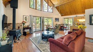 A spacious living room with a high ceiling, a fireplace, a sofa, and a dining area with a view of the outdoors. - Groveland Vacation Rental ~ 26 Miles to Yosemite! (Groveland)