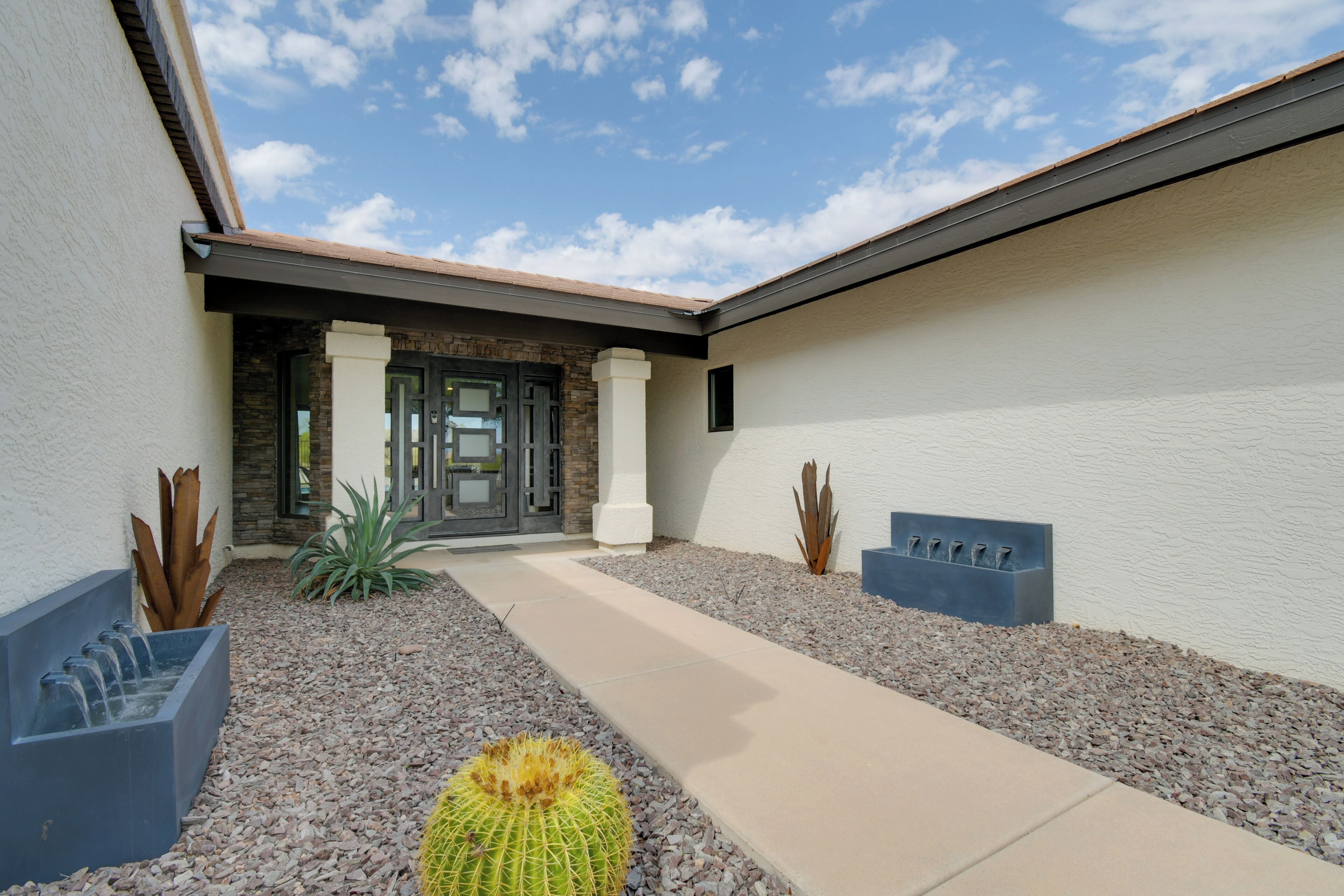 A modern building with a stone facade, a concrete planter with a cactus, and a pathway leading to the entrance.