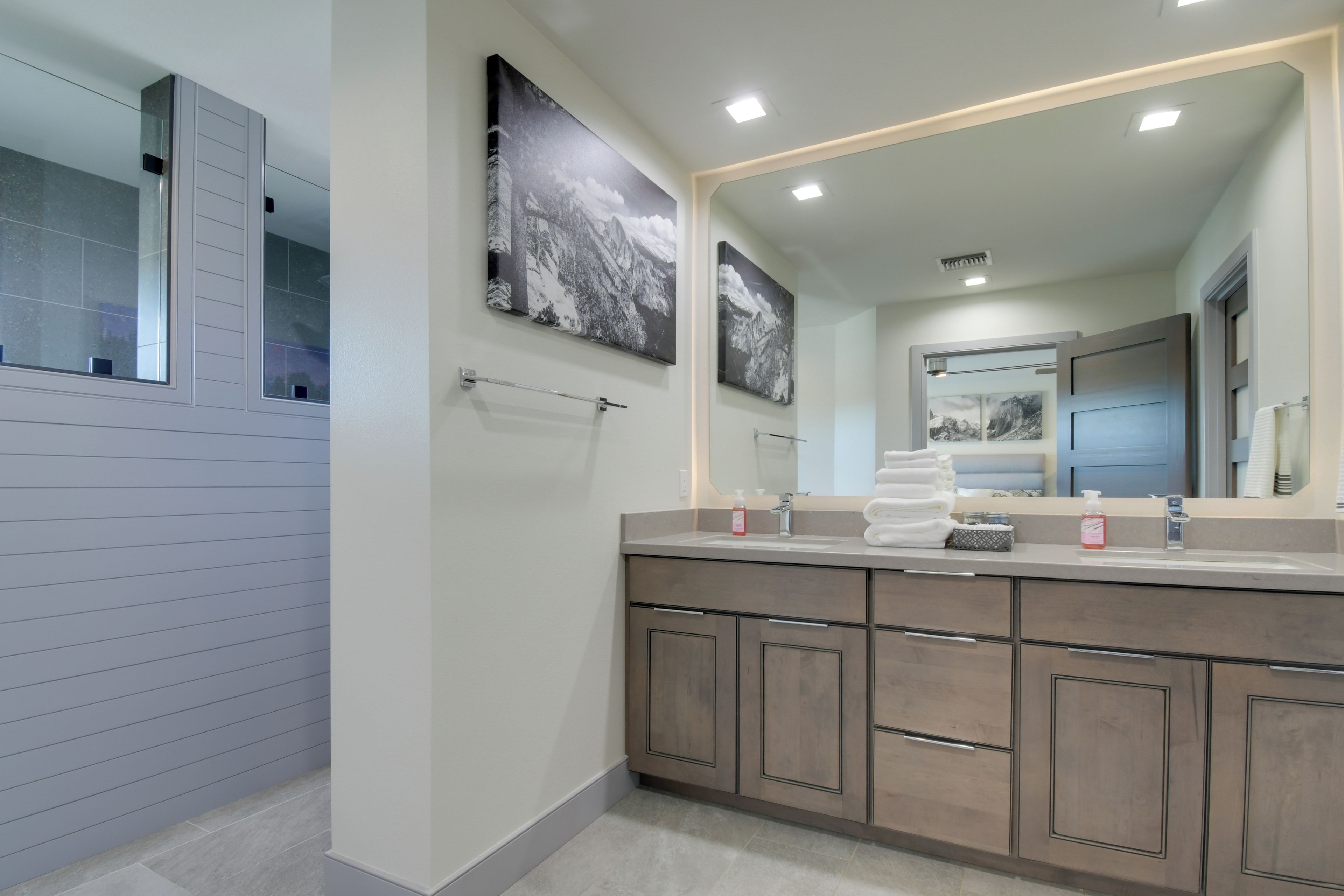A modern bathroom with a large mirror, two framed pictures, and a vanity with a towel rack.