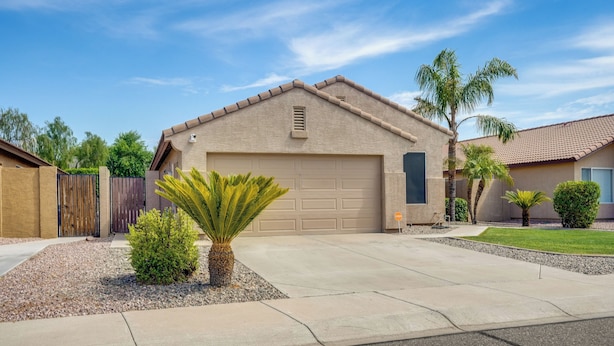 A residential house with a garage, a driveway, and a small garden with palm trees. - Bright Peoria Home w/ Gas Grill & Fire Pit! (Peoria)