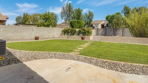 A backyard with a paved patio, a well-maintained lawn, a stone pathway, and a tall privacy fence. - Bright Peoria Home w/ Gas Grill & Fire Pit! (Peoria)