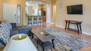 A living room with a sofa, a coffee table, and a TV. There is a kitchen in the background with a dining area. - Bright Peoria Home w/ Gas Grill & Fire Pit! (Peoria)