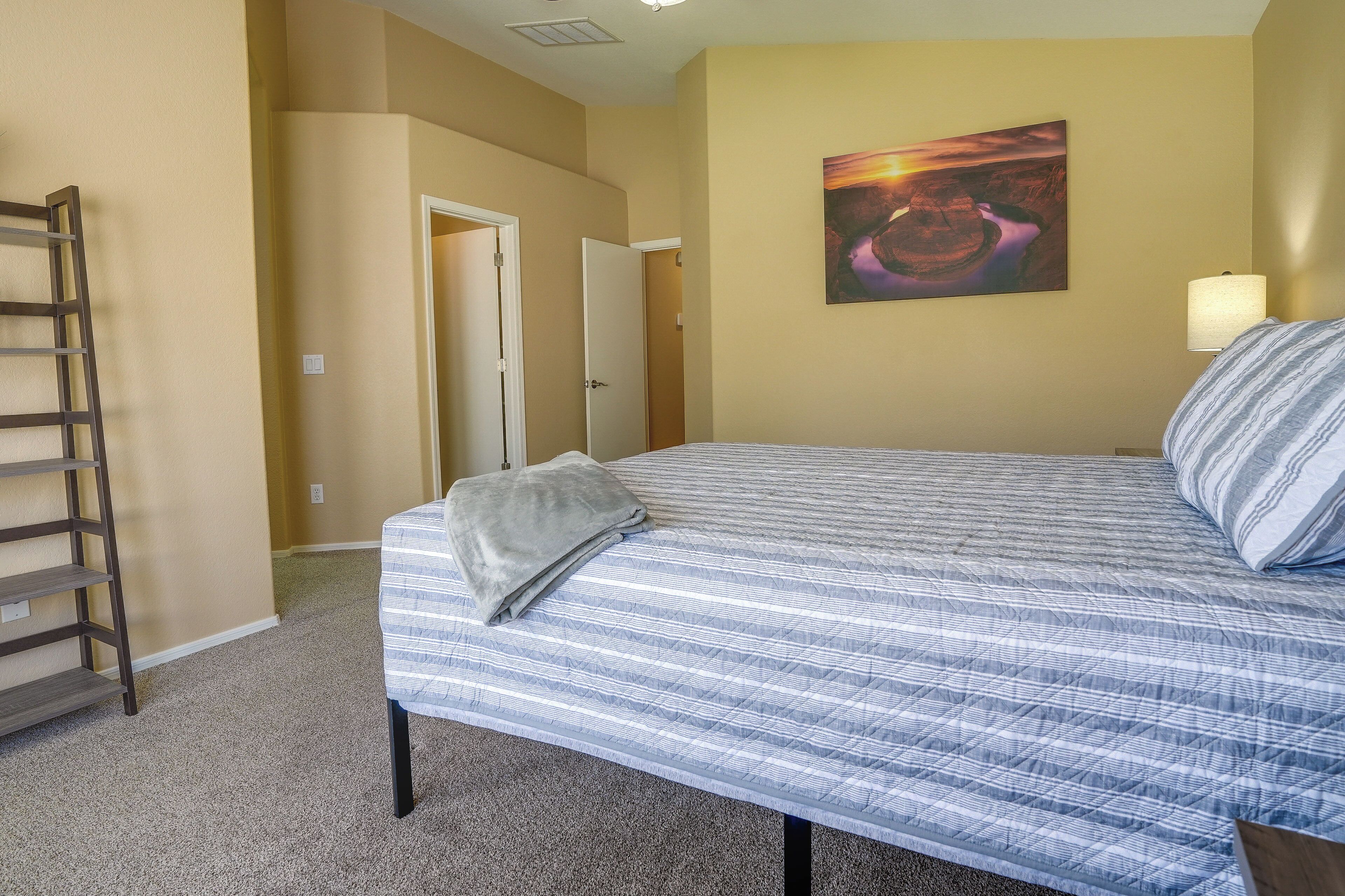 A bedroom with a bed, a painting on the wall, and a door leading to another room.