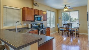 A kitchen with wooden cabinets, a microwave, and a stove. There is a dining area with chairs and a table. - Bright Peoria Home w/ Gas Grill & Fire Pit! (Peoria)