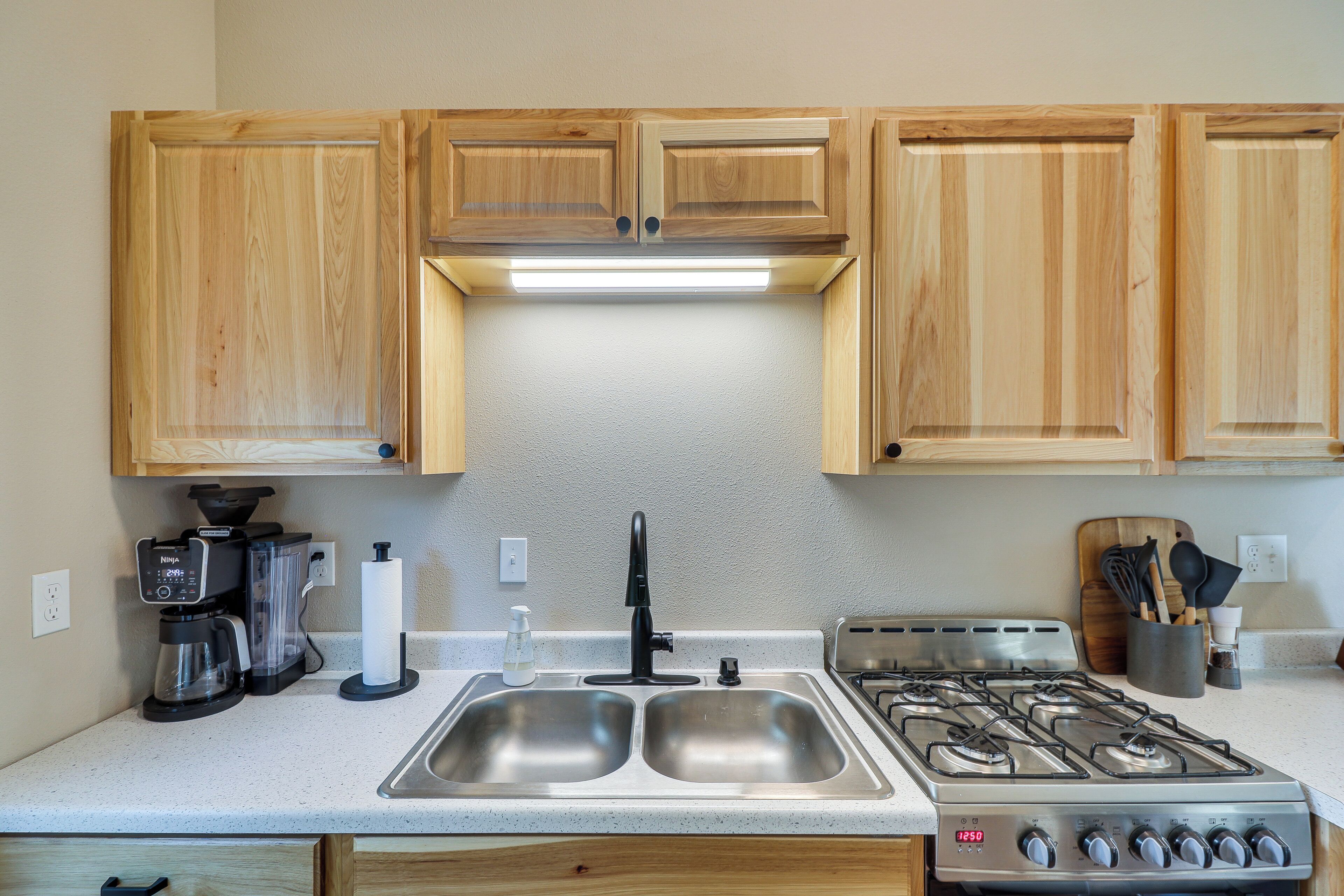 A kitchen with wooden cabinets, a stainless steel sink, a gas stove, a coffee maker, and a knife block.