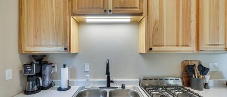 A kitchen with wooden cabinets, a stainless steel sink, a gas stove, a coffee maker, and a knife block.