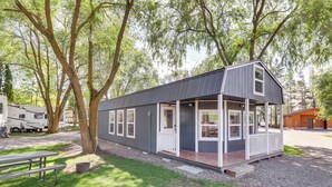 A small, single-story cabin with a porch, surrounded by trees.