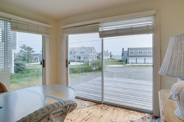 A room with a glass door leading to a deck, a wicker chair, and a table.