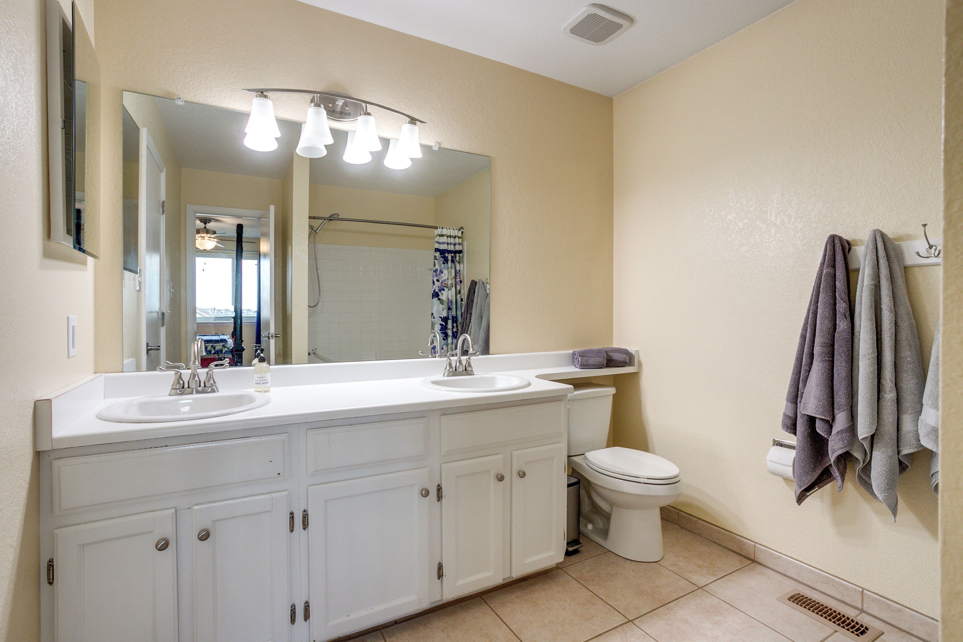 A bathroom with a white sink, mirror, and toilet. There are towels hanging on the wall and a shower curtain.