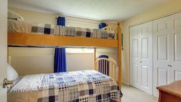 A bunk bed room with a checkered bedspread, a window with blue curtains, and a white door.