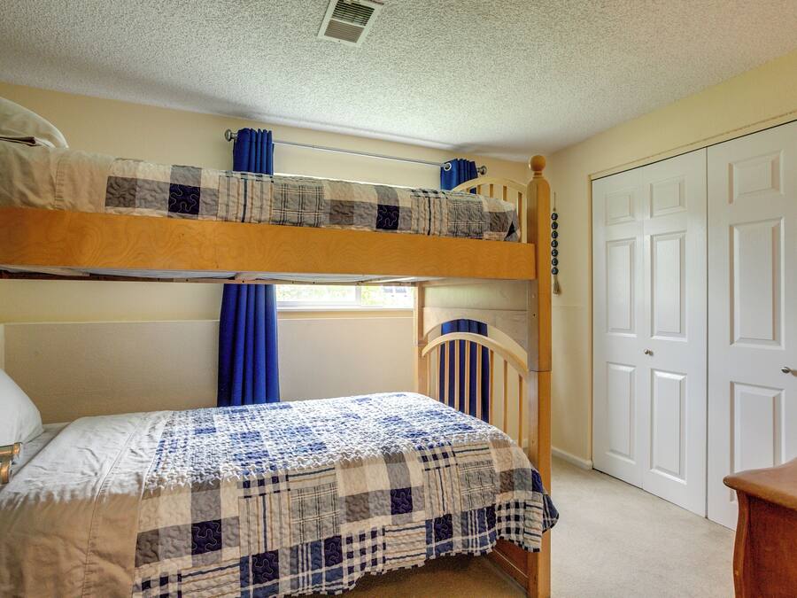 A bunk bed room with a checkered bedspread, a window with blue curtains, and a white door.