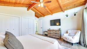 A bedroom with a large bed, wooden ceiling beams, a flat-screen TV, a white armchair, and a dresser. - Pet-friendly Monterey Home 2 Mi to Beach (Monterey)