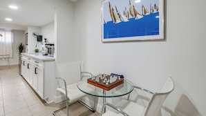 A modern kitchen with white cabinets, a glass dining table, and a framed painting of sailboats.