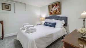 A neatly made bed with folded towels, a bedside lamp, and a painting above it.