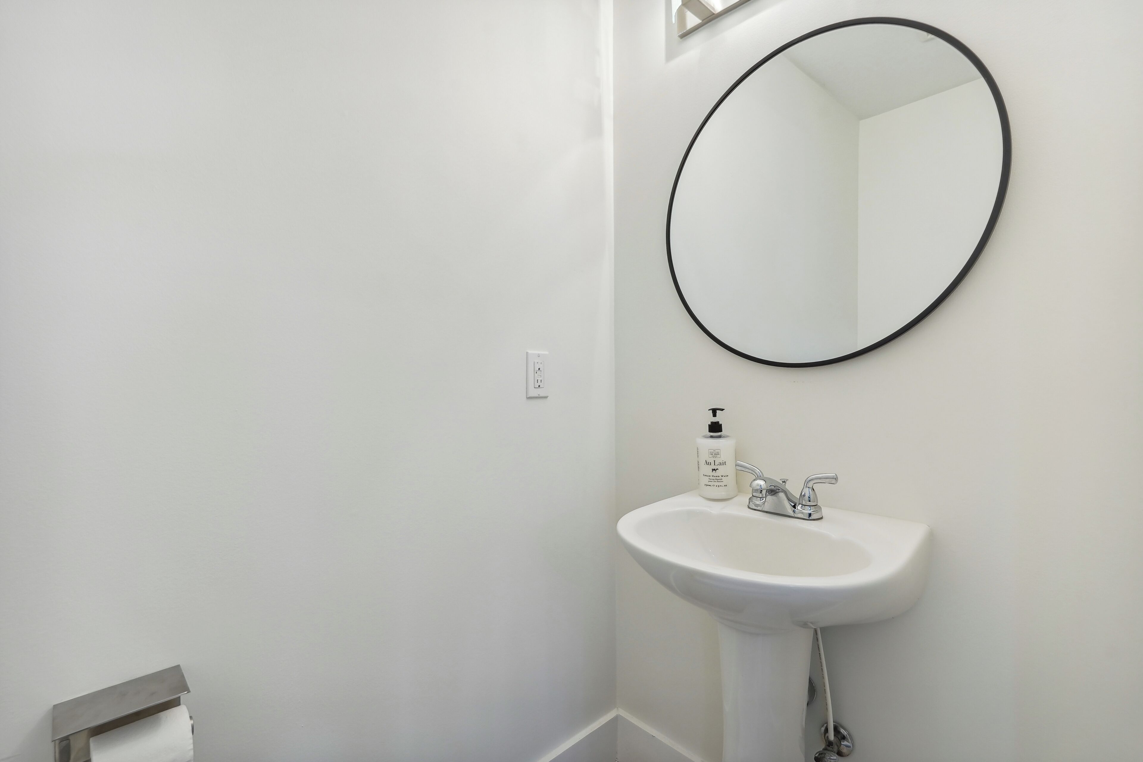 Een badkamer met een witte wastafel, een spiegel en een toiletrolhouder.
