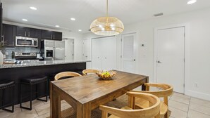 Una cocina moderna con armarios oscuros, electrodomésticos de acero inoxidable y una mesa de comedor de madera con sillas.
