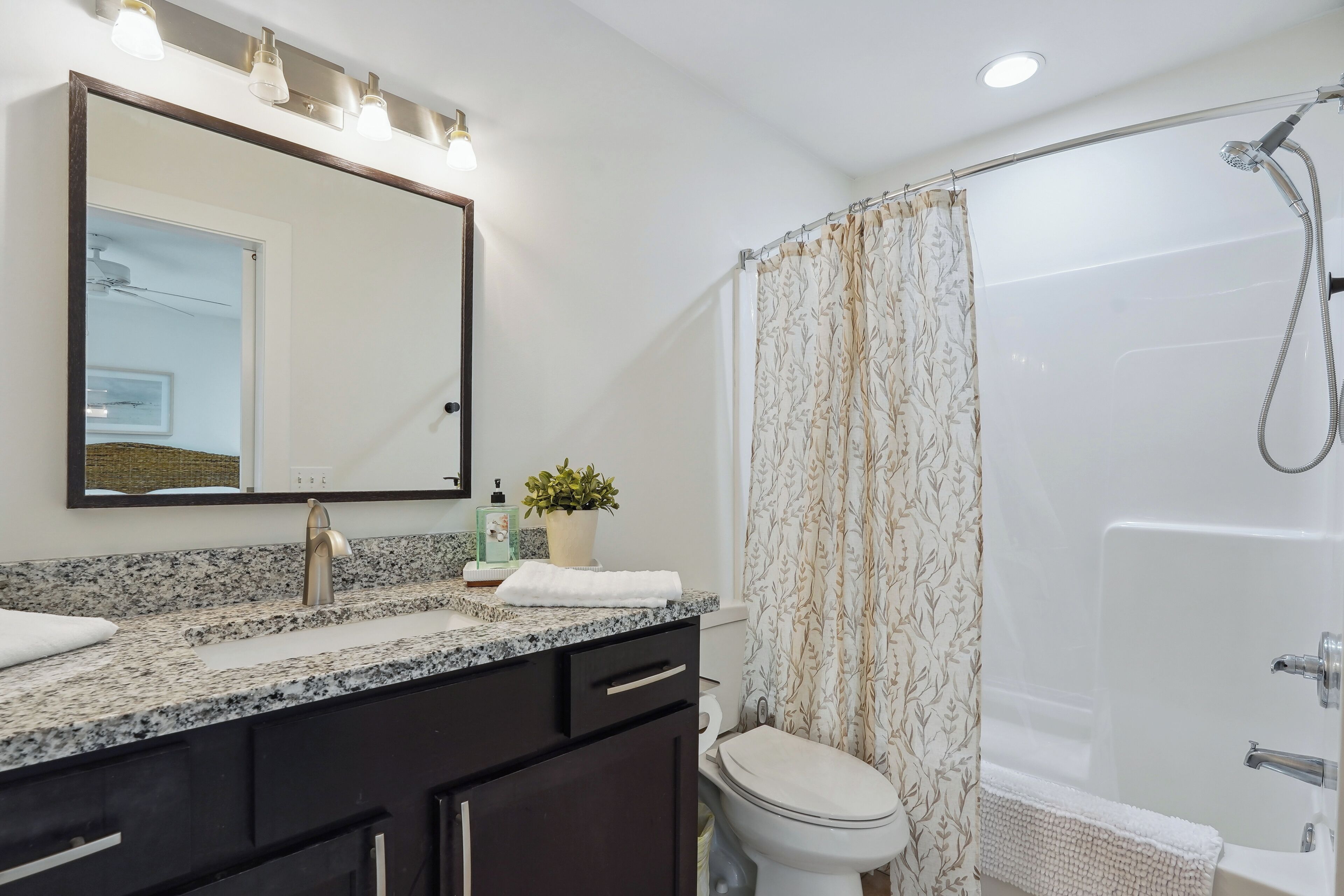 Une salle de bain avec un comptoir en granit, un lavabo, des toilettes, une douche avec un rideau et un miroir avec éclairage.