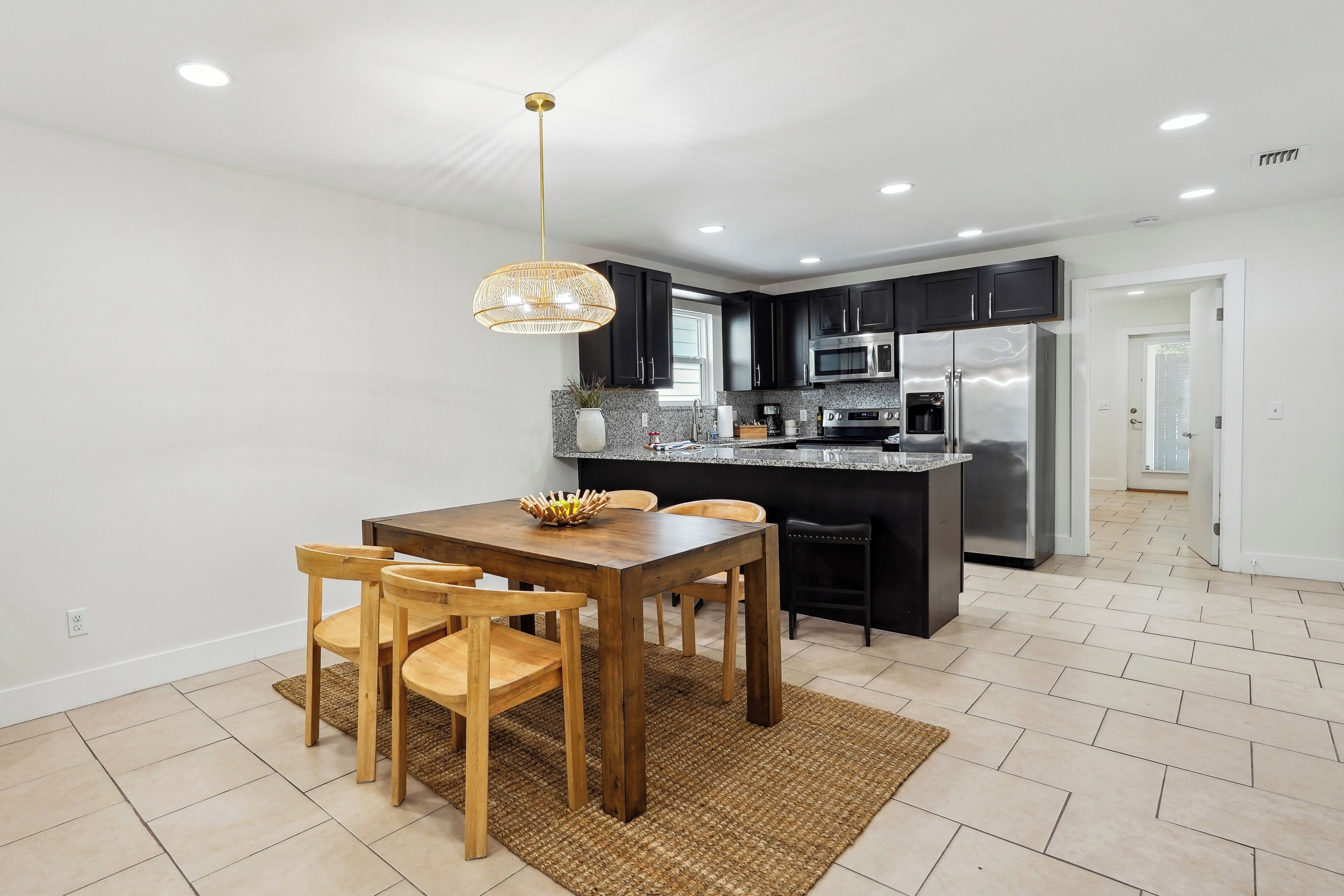 Una cocina moderna con armarios oscuros, electrodomésticos de acero inoxidable y una mesa de comedor de madera con sillas.