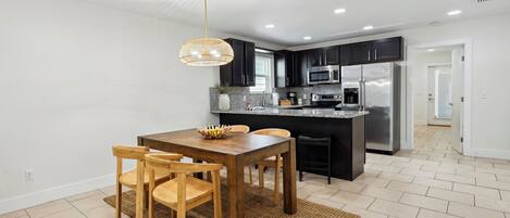 Una cocina moderna con armarios oscuros, electrodomésticos de acero inoxidable y una mesa de comedor de madera con sillas.