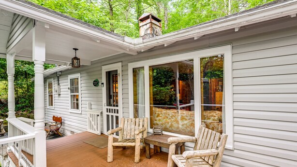 A covered porch with wooden chairs and a table, surrounded by white siding and a stone chimney. - Highlands Vacation Rental - Walk to Mirror Lake! (Highlands)