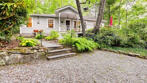 A rustic cabin with a porch, surrounded by lush greenery and a gravel driveway. - Highlands Vacation Rental - Walk to Mirror Lake! (Highlands)