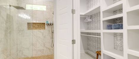 A modern bathroom with a glass-enclosed shower, white tiled walls, and a built-in shelving unit with patterned tiles.