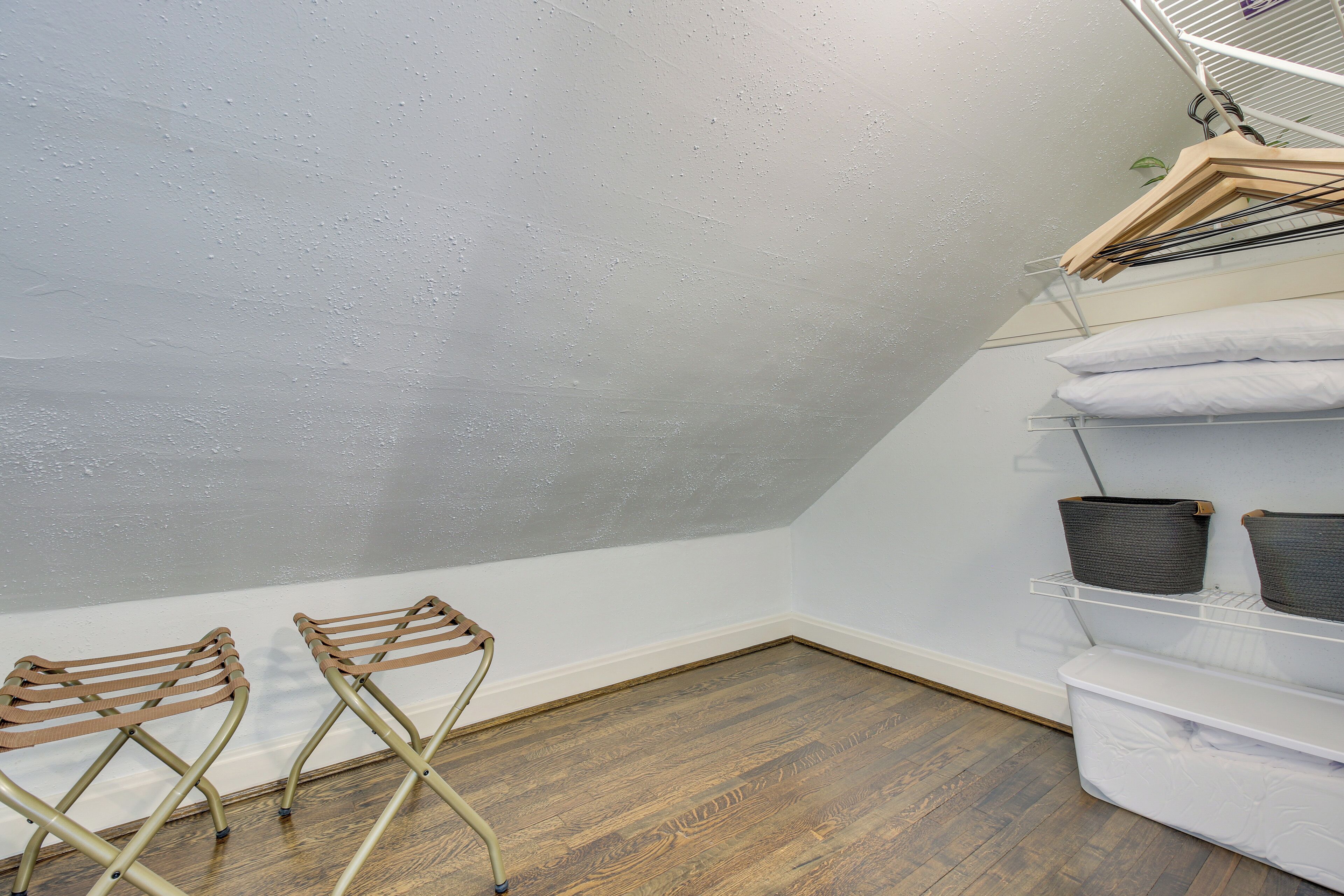 A laundry area with drying racks, shelves with baskets, and a white mattress on the floor.