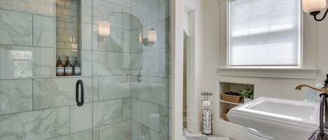 Un baño con ducha de vidrio, un lavabo blanco y una ventana con persianas.