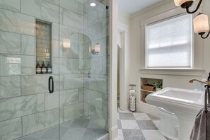 Un baño con ducha de vidrio, un lavabo blanco y una ventana con persianas.