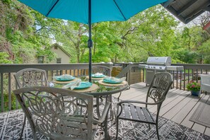 Relax outdoors with a round table and four chairs, surrounded by a wooden railing and a fence, with a grill on the deck nearby.