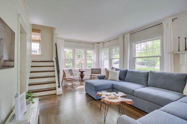 A spacious living room with a large grey sectional sofa, a wooden coffee table, and a staircase leading to another level.