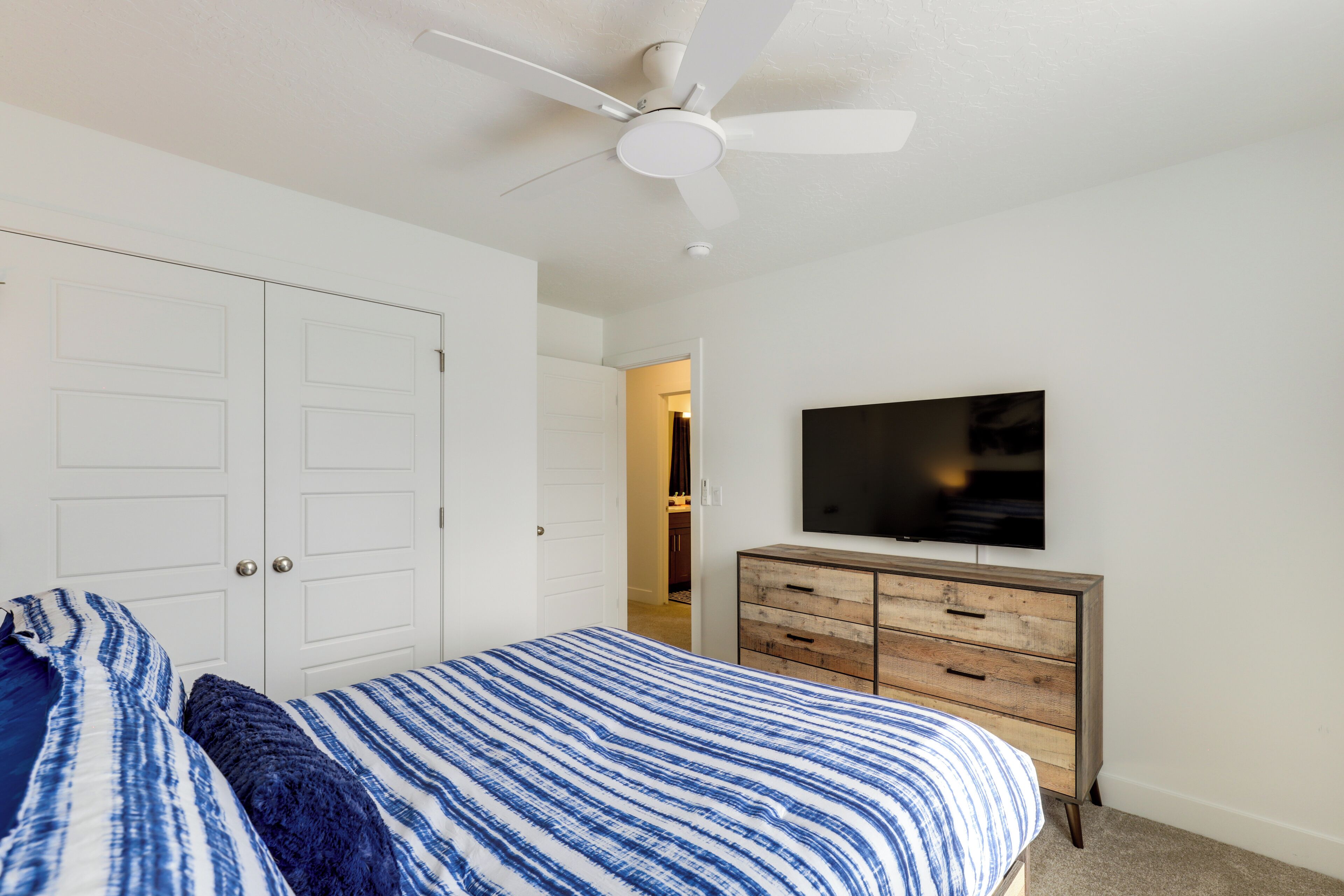 A bedroom with a bed, a ceiling fan, a dresser, and a TV on the wall.