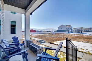 A covered porch with Adirondack chairs, a fire pit, and a view of a residential area with houses and mountains in the background.