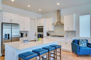 A modern kitchen with white cabinetry, stainless steel appliances, a central island with bar stools, and a blue accent chair.