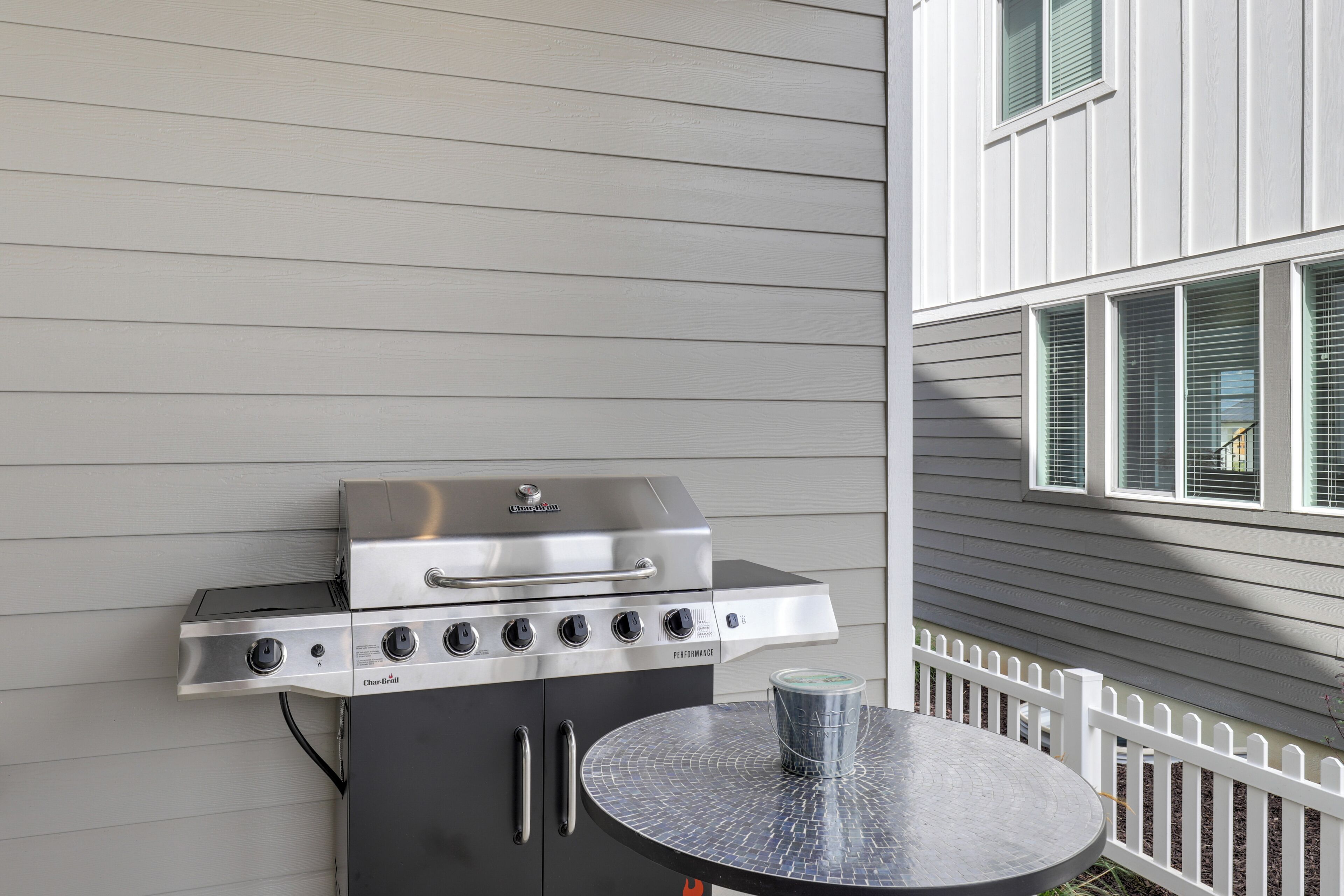 A barbecue grill with a control panel, a table with a metal top, and a white picket fence.