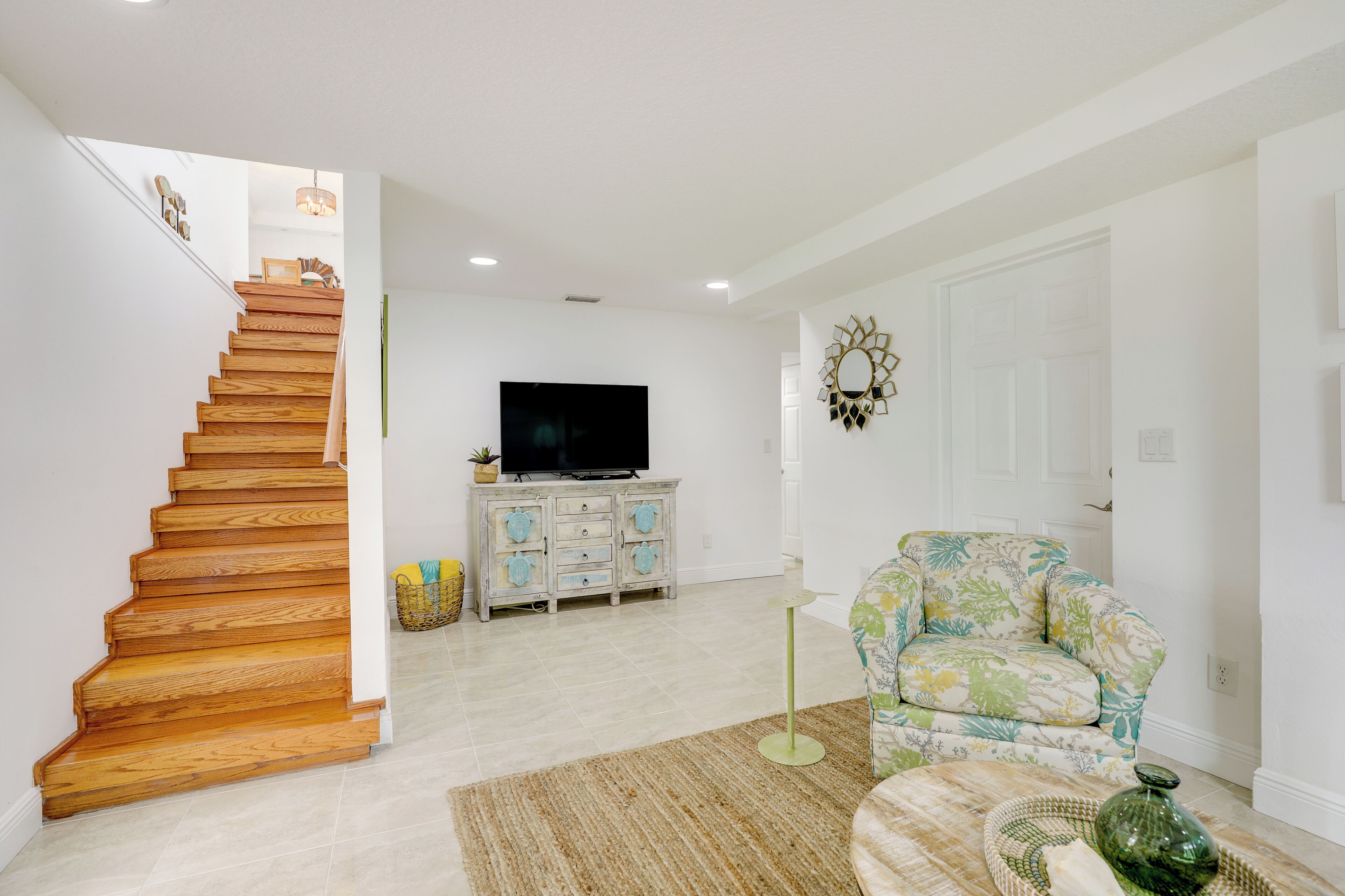 Una escalera conduce a una sala de estar con televisor, un sillón estampado y un espejo decorativo.