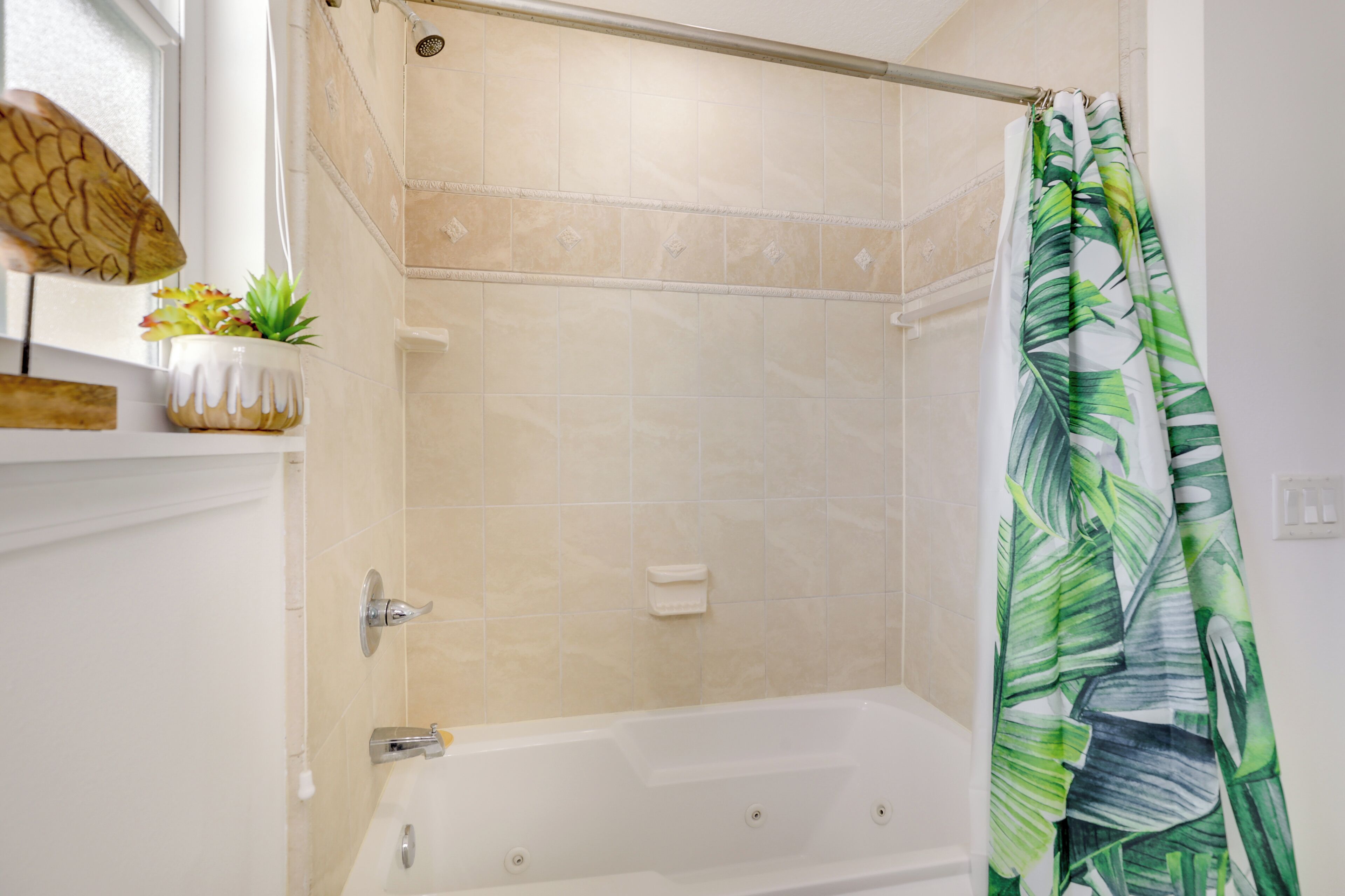 A bathroom with a bathtub, shower curtain, and a shelf with a plant.