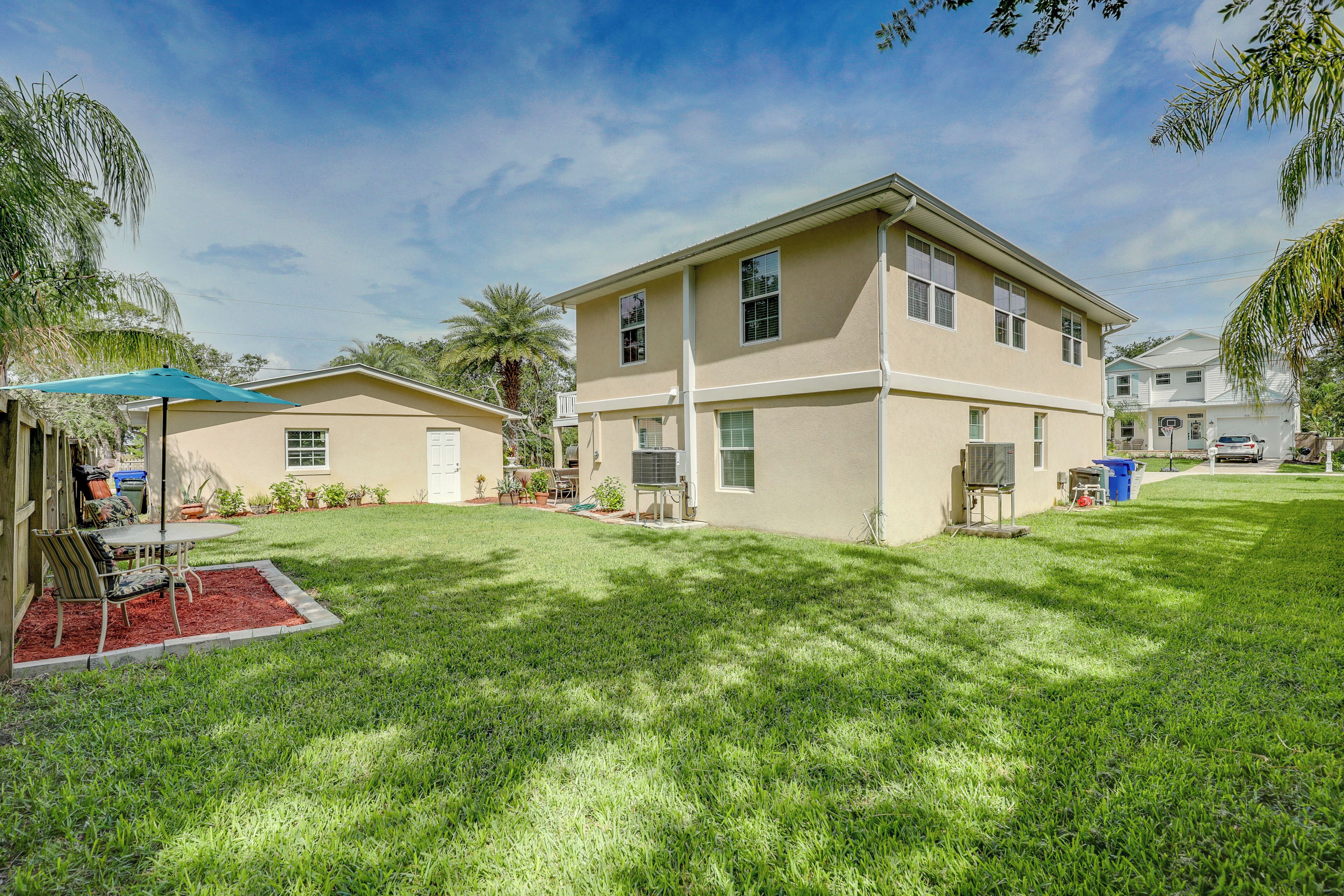 A two-story house with a well-maintained lawn, a patio with outdoor furniture, and a clear blue sky.