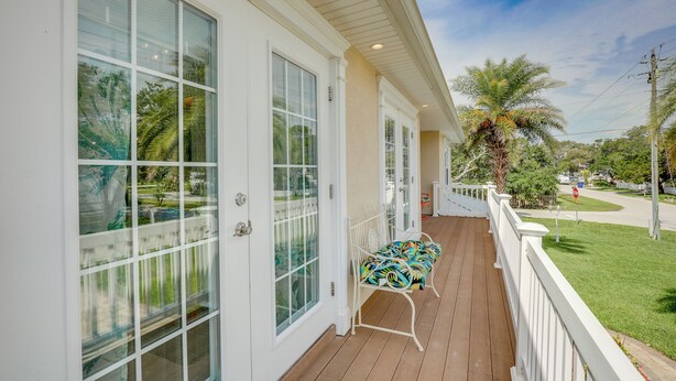 A covered porch with a white railing, a bench, and a view of a residential street with palm trees and a clear sky. - St Augustine Home Near Vilano Beach: Pets Welcome! (St. Augustine)
