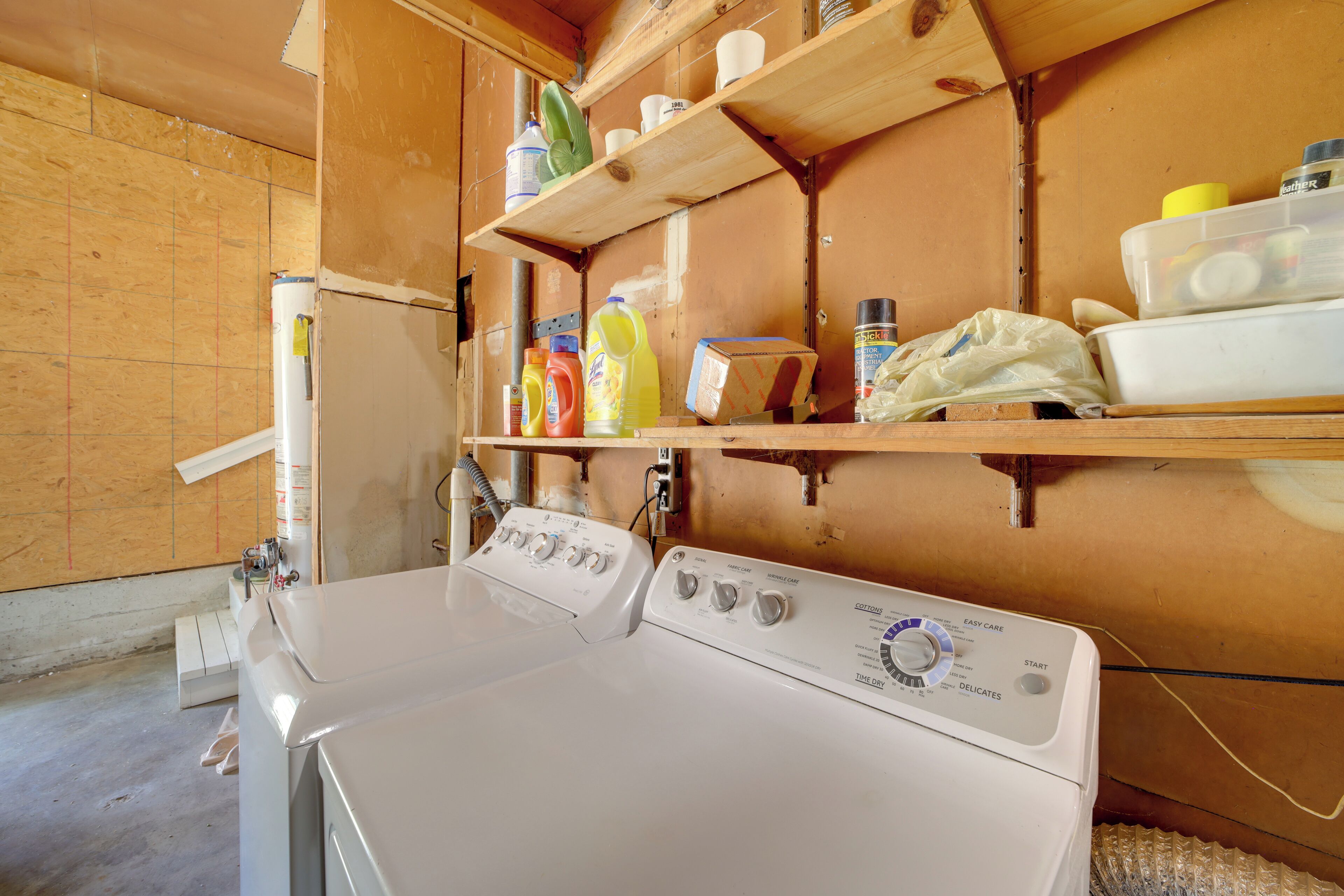 A laundry area with a washing machine, shelves with cleaning supplies, and a wooden wall.