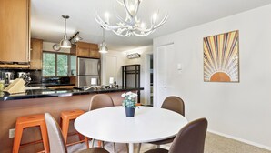 A modern kitchen with wooden cabinets, a stainless steel refrigerator, and a dining area with a round table and brown chairs.