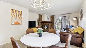 A living room with a round dining table, brown leather sofa, and a fireplace.