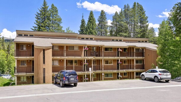 A multi-story hotel with balconies, a parking lot, and a mountainous backdrop.