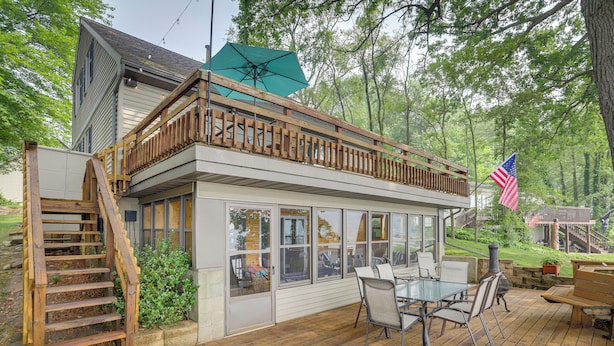 A covered deck with a glass enclosure, wooden railing, and outdoor furniture.