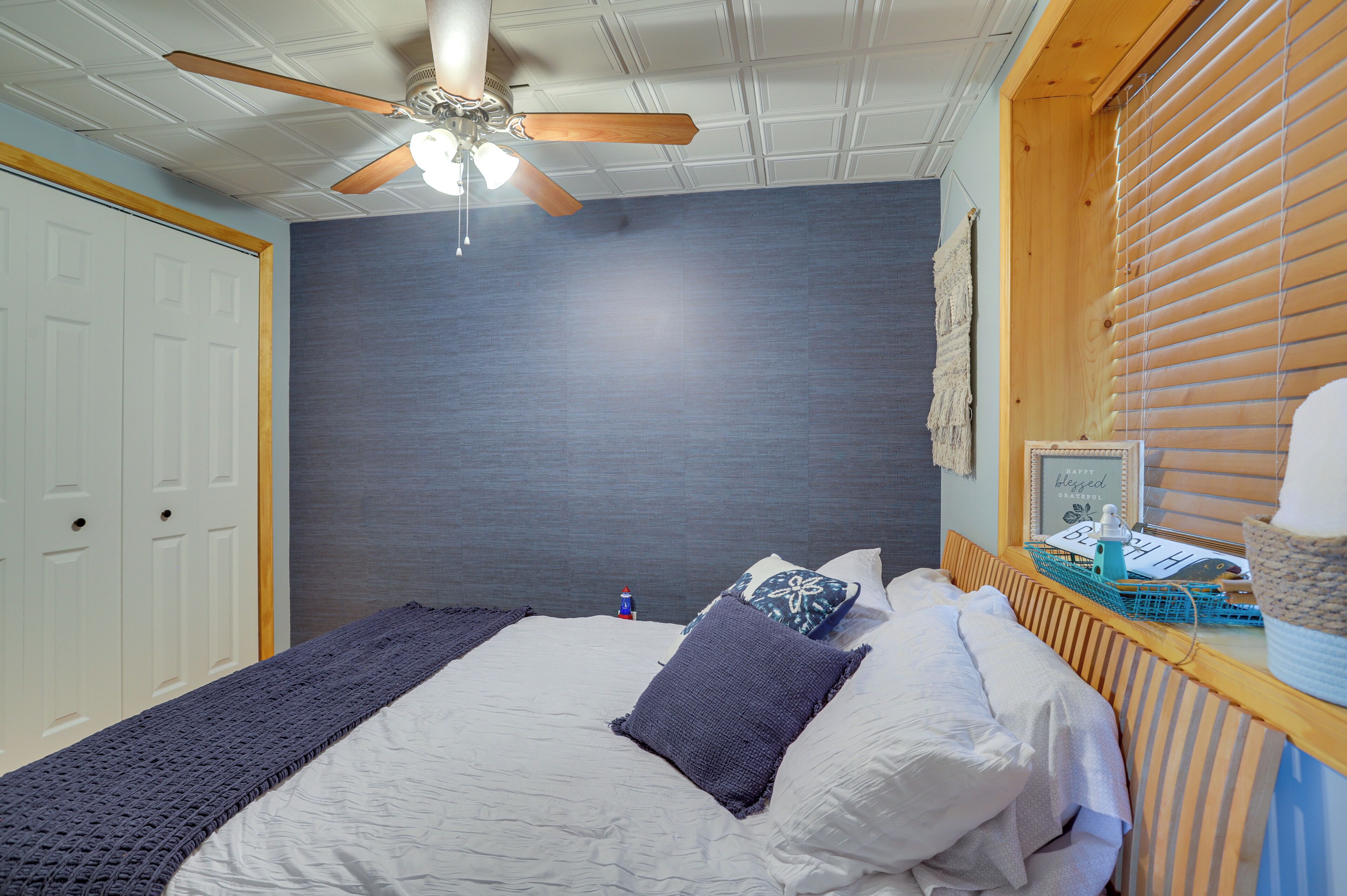 Ein Schlafzimmer mit Bett, Deckenventilator, Fenster mit Jalousien und einer Wandleuchte.