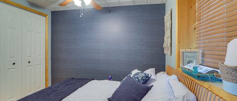 Ein Schlafzimmer mit Bett, Deckenventilator, Fenster mit Jalousien und einer Wandleuchte.