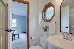 A bathroom with a white sink, a mirror, and a toilet. There is a wooden door leading to another room. - Lakefront Sister Lakes Vacation Rental w/ Dock! (Dowagiac)