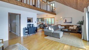A spacious living area with a high ceiling, wooden beams, a balcony, a kitchen, and a dining area.