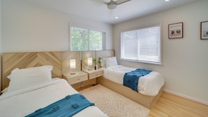 Ein Schlafzimmer mit zwei Betten, einem Deckenventilator und zwei Fenstern mit Jalousien.